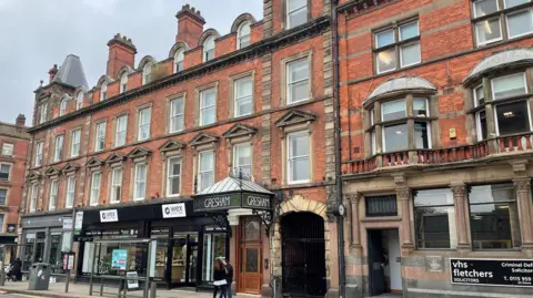 Historic England Carrington Street showing a row of four-storey brick shops, including a hotel with a Victorian iron canopy