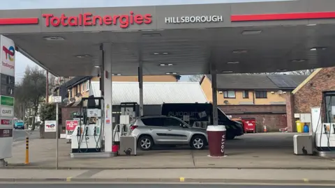 Simon Thake A forecourt of a petrol station showing several pumps and a car and van parked up.
