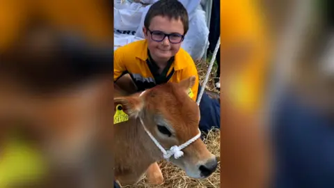Smiling boy with glasses posing with a young calf