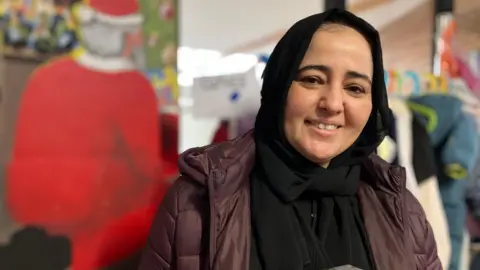 A woman wearing a headscarf and a purple puffer coat with Santa in background.