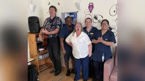 Essex Partnership University NHS Foundation Trust Marcus Brown performing with a guitar at Clifton Lodge, with staff joining in to sing for residents and their families