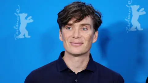 Getty Images Cillian Murphy wearing a navy shirt smiling against a blue backdrop 