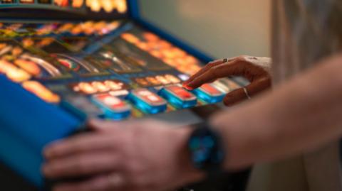A close up image of hands at a fruit machine in a gambling shop