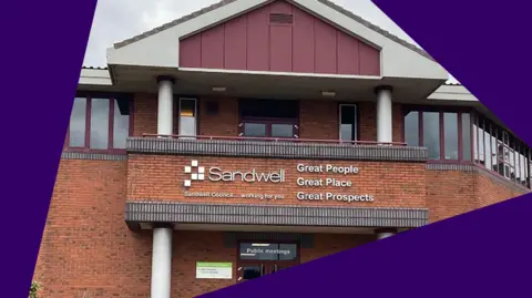 Local Democracy Reporting Service A redbrick two-storey building with a triangular roof. The building has windows all along the top floor, which have maroon window frames. The building says "Sandwell" in large white letters on the front.