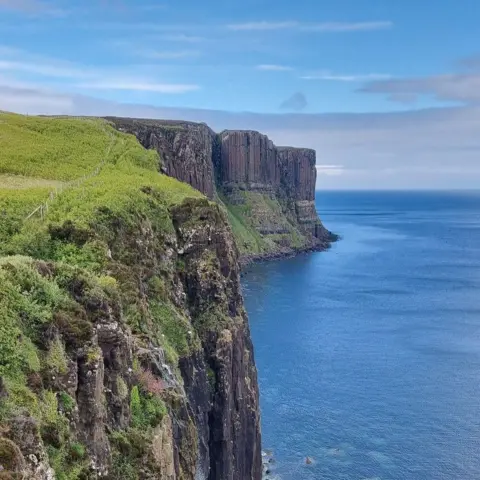 Mangela Coia Cliffs in Skye with a straight sheer drop down into the water. The cliffs are topped with bright green grass.