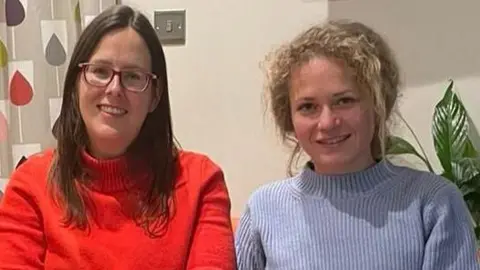 Sarah Kinch Two women, Sarah and Yulia, sitting side by side, smiling at the camera