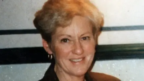 A physical photograph of Mrs Speakes. She has short blond hair, hoop earrings, and is smiling at the camera.