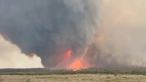 A dark cloud of smoke with a column of fire at its centre rises into the sky.