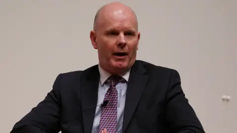 Brian Lawless/PA Wire A man in a black suit with a blue shirt and red patterned tie. He is bald.