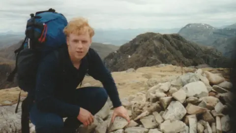 Roddy Russell A photo of Rob on a hilltop. He is wearign dark blue clothing and is carrying a backpack