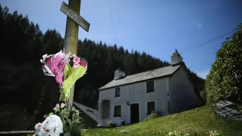 Getty Images A teddybear and floral tributes adorn a post outside of the former home of Mark Bridger in Ceinws, Mid Wales who was convicted of the abduction and murder of April Jones in 2013 in Machynlleth, Wales. The jury trying Bridger visited key scenes in Machynlleth following the disappearance of five-year-old April Jones. 
