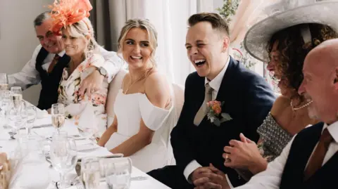 Head table at a wedding with bride and groom laughing along with both sets of parents