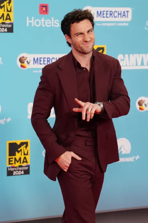 PA Media Aaron Taylor-Johnson winking and pointing in a burgundy suit