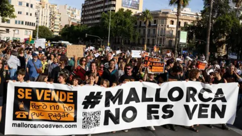 Getty Images Protesters hold a banner reading "Mallorca is not for sale" during a demonstration to protest against the massification of tourism and housing prices on the island of Mallorca in Palma de Mallorca 