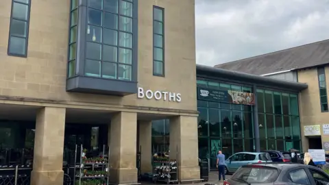 A supermarket with brick walls and large glass windows. There are cars parked outside