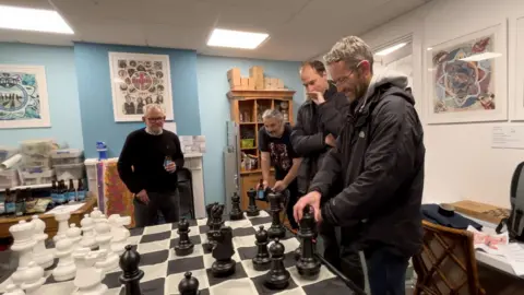 bbc Men play chess on a large board together 