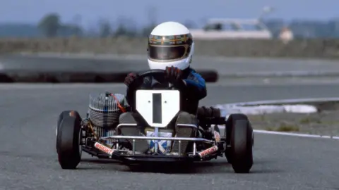 Getty Images A young Allan McNish in a racing kart with the number 1 on the front. He has a white helmet on with a tartan trim.