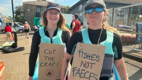BBC Two women with anti-sewage placards hanging over their torsos take part in a Surfers against Sewage protest in Bristol
