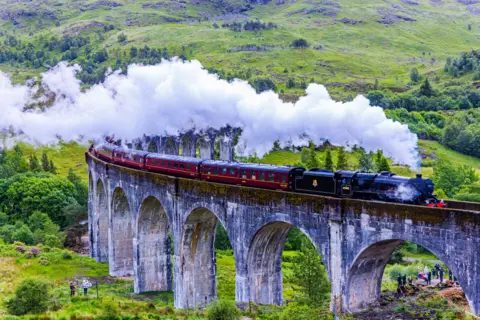 Mike Connor Steam train crossing a curved viaduct with steam billowing behind it.
