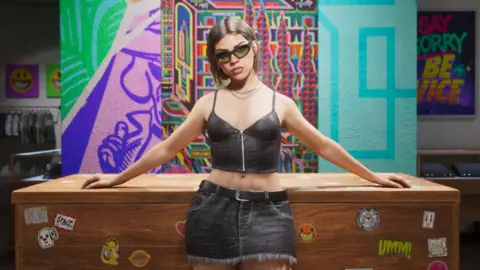 An in-game screenshot from GTA 6 showing a woman inside a shop in a short black top and a skirt with her arms resting on a desk behind her and a colourful background. She is wearing black sunglasses and has short brown hair. 