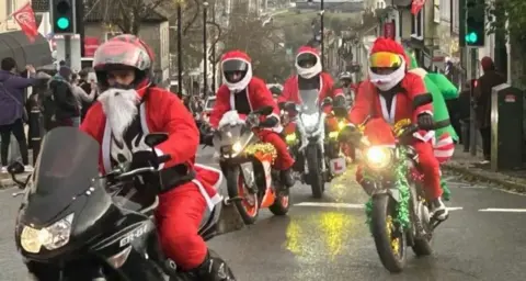 A group of motorcylists dressed in Santa suits with tinsel on their bikes.