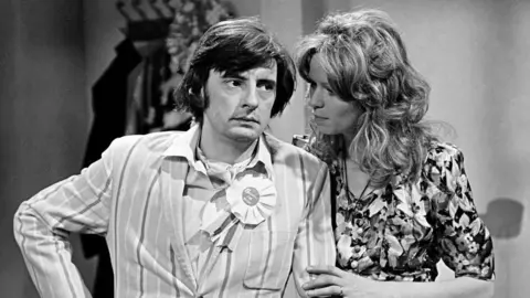 A man and a woman stand in conversation. 