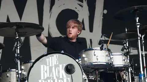 Getty Images Bryar sitting behind a set of drums looking off to one side as he drums at the Sydney leg of the Big Day Out Festival in January 2007 . A large drum at the front has the words The Black Parade on it 