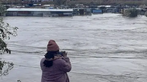 A woman takes pictures in front of a flooded body of water in South Africa's Eastern Cape province