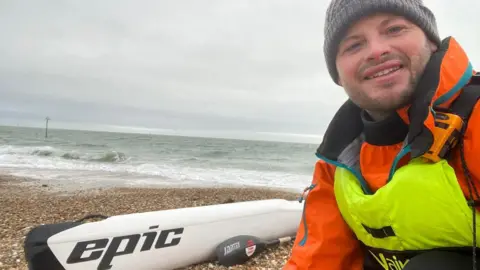 Mike Lambert Mike Lambert on the beach, next to a kayak