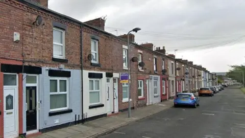 A row of terraced houses, with a line of cars parked on the side of the pavement 