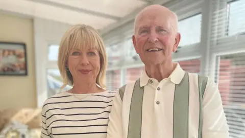 BBC Marie-Louise Connolly and her dad Joe. Marie-Louise is wearing a striped white and black top and her dad is wearing a striped green and cream top. He has grey hair and she has blonde hair. Both have blue eyes.