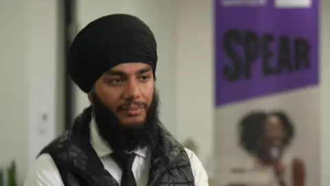 A young man in beard and turban looking serious. He is wearing a white shirt and tie