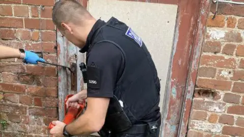 Devon County Council Police officer breaking down door in shop raid