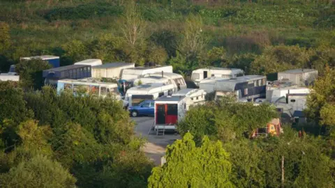 Getty Images Roughly a dozen caravans and vehicles parked in a car park. The car park is surrounded by green fields and trees.