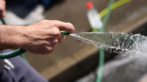 A male hand holds the end of a hosepipe as water gushes out.