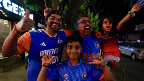 EPA/Shutterstock Two men and two children - of which three are wearing the blue jersey of the India men's cricket team - celebrate India's victory in the T20 cricket World Cup in the southern city of Bangalore on 8 March 2026.