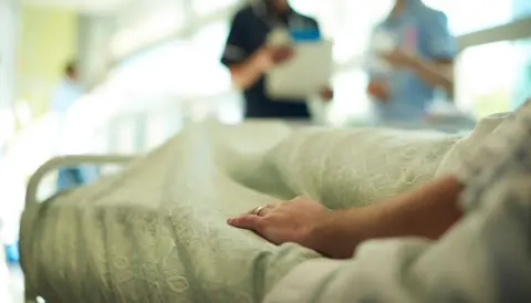 Getty Images Patient lying in a bed while medical staff talk in background