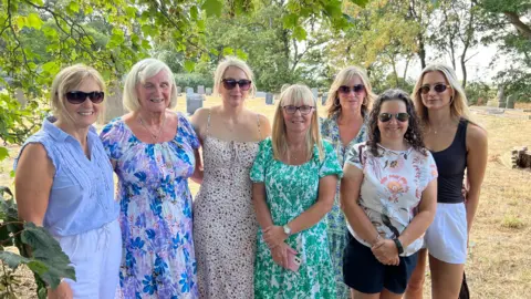 Siete mujeres están de pie juntas en el cementerio de la iglesia de San Martín y miran a la cámara.