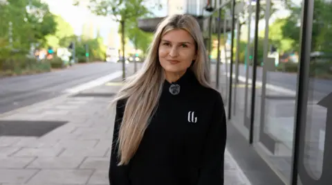 Dagy, 21, who's a student, stands in a street in Nottingham. She has blonde hair and is wearing a black top