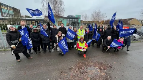 Stuart Woodward/BBC A group of people in winter clothing holding union flags outside a school fence.