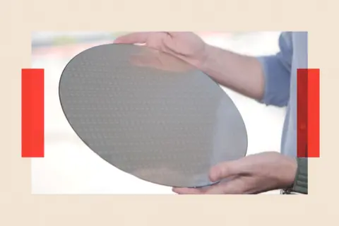 A person holds a silicon wafer, which looks like a thin silver disc