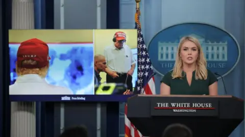 Reuters Trump watches airstrikes, wearing a red hat and a headset over his ears. The photo is shown in the White House briefing room