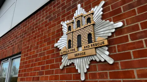 A large Suffolk Fire and Rescue Service emblem on the side of a brick building.