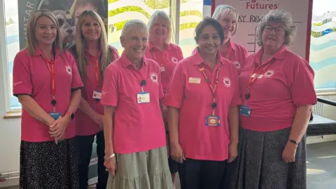 Seven women, all wearing pink polo shirts, standing together smiling into the camera.