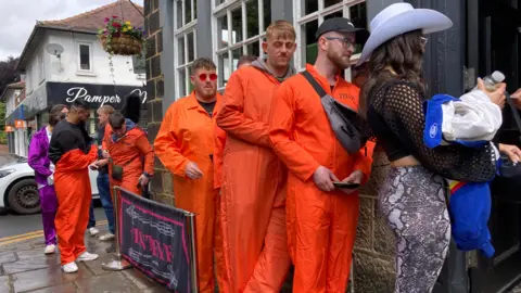 BBC/Carla Fowler People wearing fancy dress queue to get in a pub