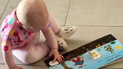 imaginationlibrary.im A young baby reading a children's book on a kitchen floor. 