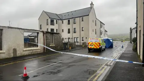 BBC Police van and police tape on road at scene of incident among houses