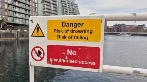 BBC Yellow sign warning "Danger - Risk of drowning, risk of falling" above a red sign warning "no unauthroised access"