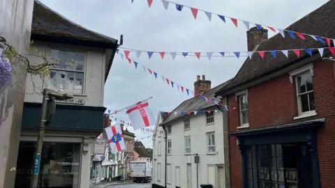 Darren Rozier/BBC Red, white and blue bunting hanging between several shops, while an England flag and the Suffolk flags hangs from a building.