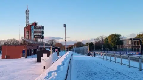 The grandstand, a large brown building, with snow around it. 